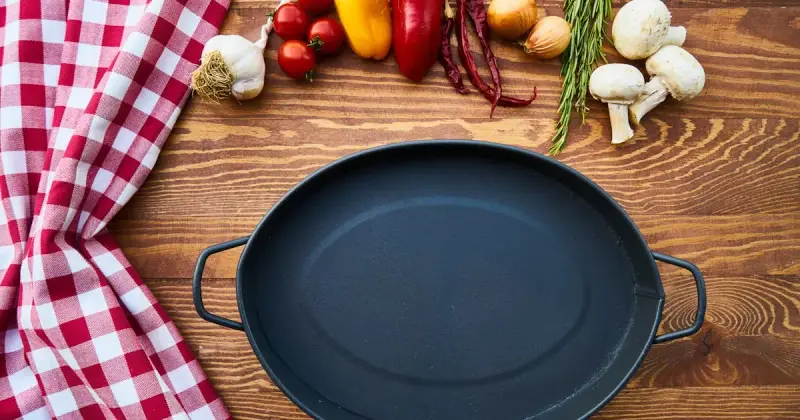 High angle of pan with fried egg with seasoning placed on wooden board in kitchen