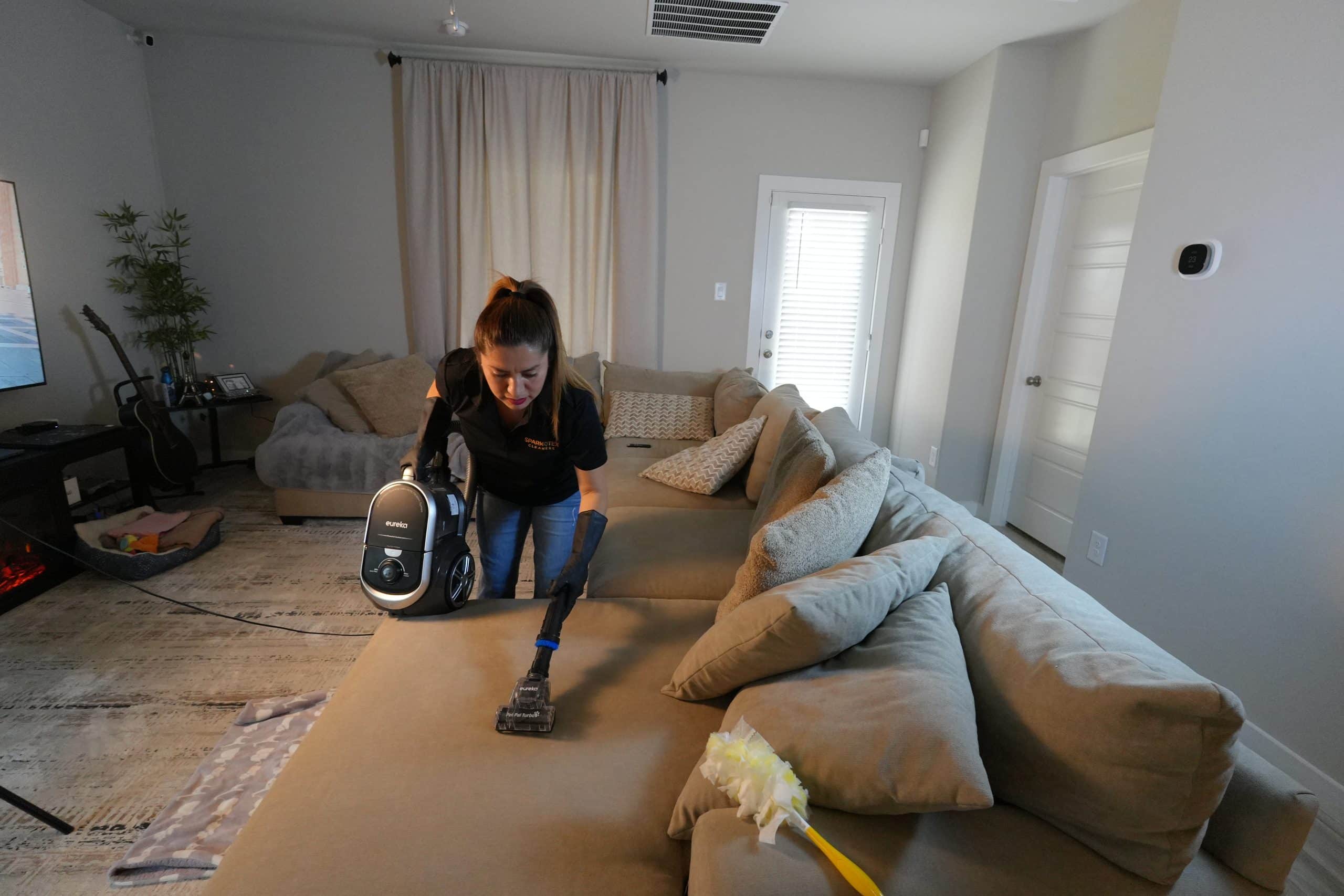 Residential Cleaning 15 Woman using a Eureka vacuum cleaner to clean a beige couch.
