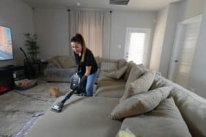 Residential Cleaning 5 House cleaner vacuuming a beige couch with a Eureka vacuum cleaner.