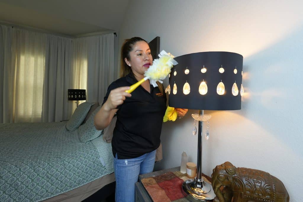 House cleaner in Conroe - dusting lampshade with feather duster