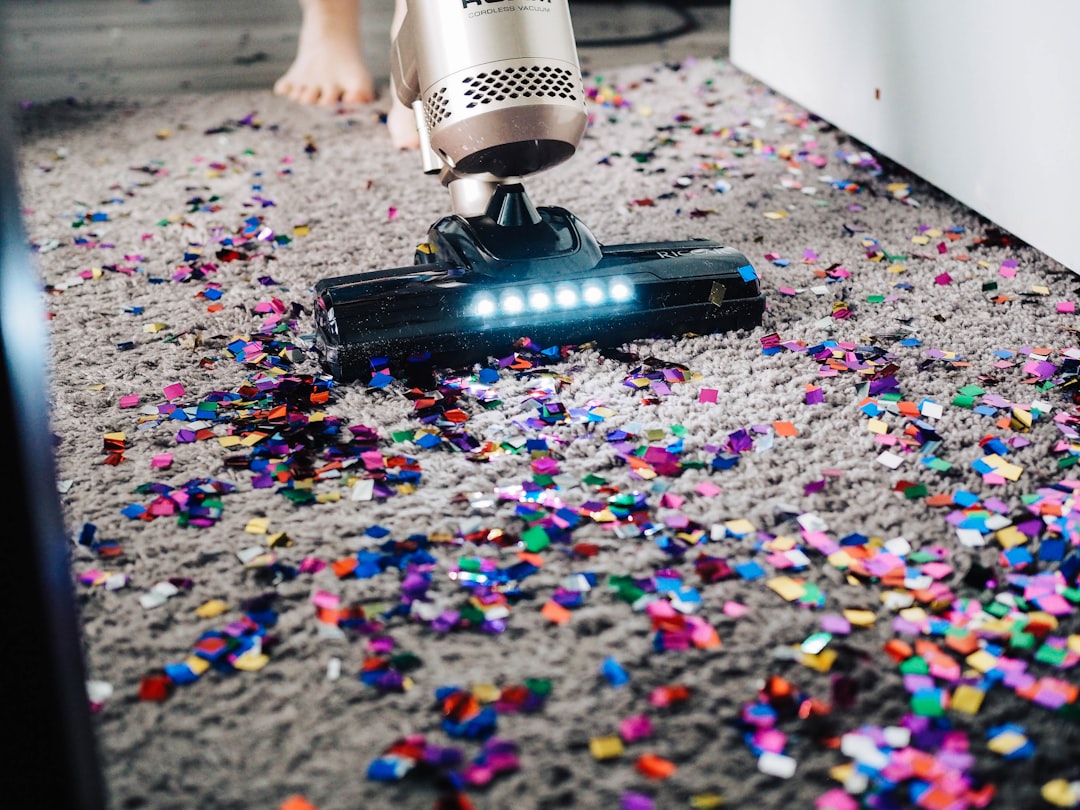 Vacuum cleaner picking up colorful confetti on carpet.