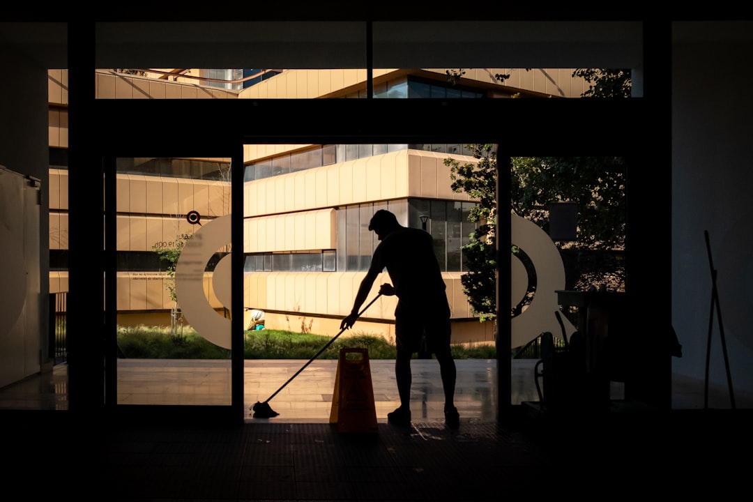 Silhouetted janitor mopping floor near modern building.