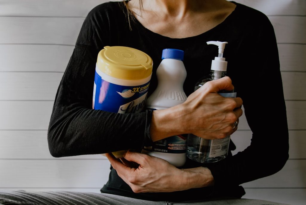 Person holding cleaning supplies, disinfectant wipes, and soap.