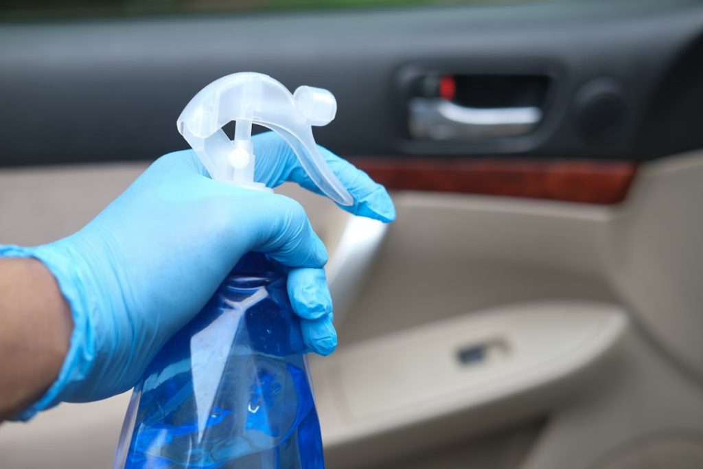 Gloved hand holding blue spray bottle in car.