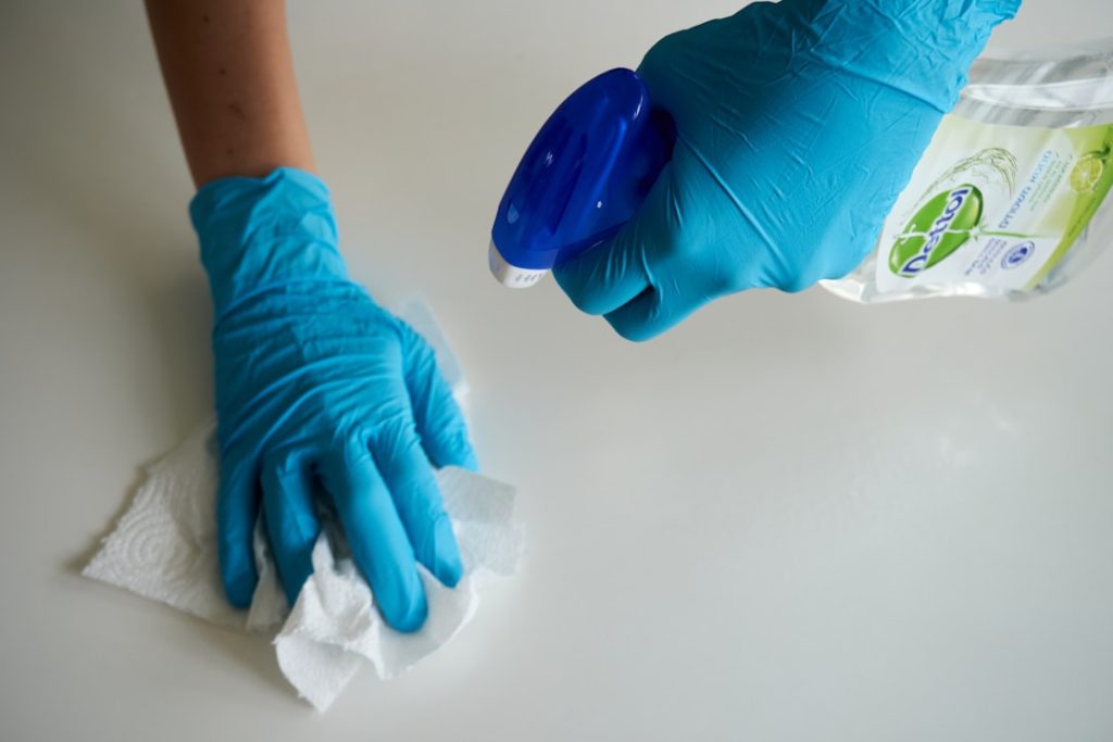 Person cleaning surface with gloves and disinfectant spray