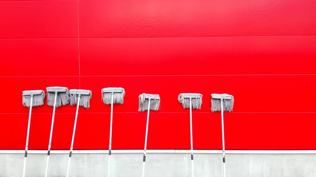 Seven mops against bright red wall background.