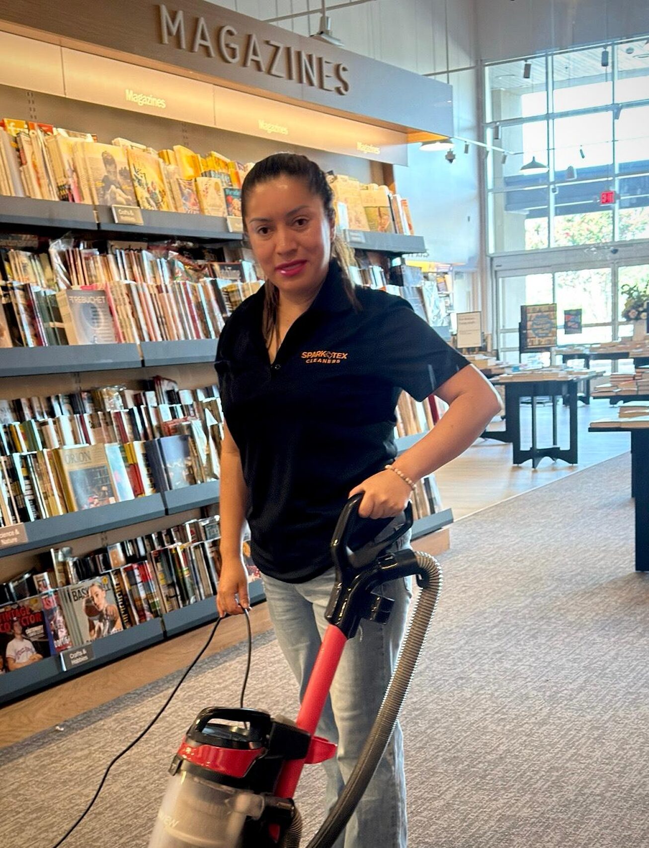 Special Offers 1 Smiling cleaning professional with vacuum, SparkTex Cleaners logo on shirt, in bookstore.