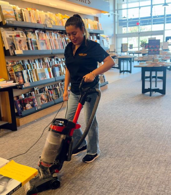 Residential photo 4 A cleaning professional vacuums the floor of a bookstore. The logo on her shirt says "Sparkle-Tex Cleaners".
